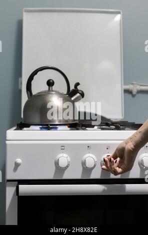 una persona aggiunge gas sul fornello dove si trova il bollitore. Foto di alta qualità Foto Stock