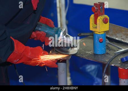 l'operatore ha le mani di smerigliare la piastra metallica con una smerigliatrice, preparandosi per la saldatura. Foto Stock