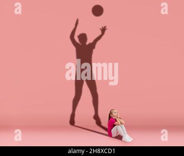 Immagine concettuale con capretto e ombra di giocatore di pallavolo femminile sulla parete dello studio. Sogni di carriera sportiva Foto Stock