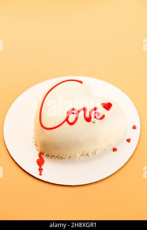 Mousse torta a forma di cuore con l'iscrizione amore su sfondo arancione per San Valentino e 14 febbraio Foto Stock