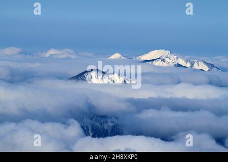 Le vette innevate della montagna si stacca dalle nuvole soffici. Sullo sfondo c'è un cielo blu chiaro. Un paesaggio invernale Foto Stock