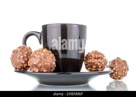 Quattro caramelle dolci al cioccolato con noci su un piatto di ceramica con una tazza, primo piano, isolato su bianco. Foto Stock