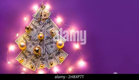 Albero di Natale fatto di 100 dollari bollette su sfondo viola con copyspace e casa chiave. Decorazione di Natale di finanza, risparmio, ricchezza, spese in ne Foto Stock