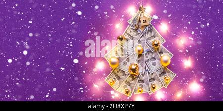 Albero di Natale fatto di 100 dollari bollette su sfondo viola con copyspace e casa chiave. Decorazione di Natale di finanza, risparmio, ricchezza, spese in ne Foto Stock