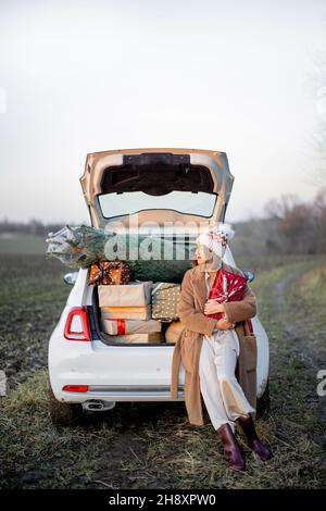 Donna e macchina piena di giftbox di Capodanno e albero di Natale Foto Stock