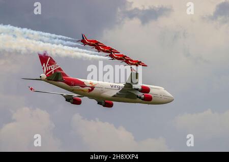 RAF Red Arrows jet che volano a fianco dell'aereo di linea Virgin Atlantic Boeing 747 Jumbo Jet G-VFAB al Biggin Hill Airshow. Scorta dell'Aeronautica reale Foto Stock