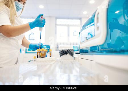 Campionamento del sangue in laboratorio. Un infermiere preleva i campioni di sangue da una provetta con una pipetta e li prepara per l'analisi. Foto Stock