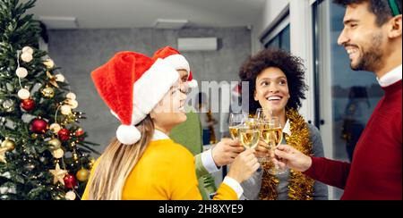 Capodanno e Natale. Un gruppo multiculturale di colleghi che si trovano in una sala riunioni e che hanno un brindisi con bicchieri di champagne a Capodanno Foto Stock