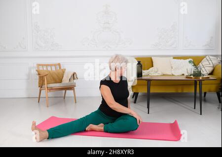 Donna sportiva anziana che fa yoga mentre guarda il tutorial sul laptop Foto Stock