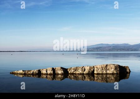 Rocce nelle acque limpide del lago Trasimeno in Italia , sullo sfondo del centro storico Foto Stock