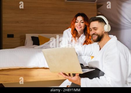 Coppia giovane in accappatoi sdraiati sul letto con un computer portatile. Uomo e donna che guardano un film. Vista dall'alto. Foto Stock