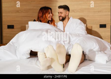 Una giovane coppia, un uomo e una donna, sono stesi in un letto vestito di accappatoi bianchi. Foto Stock