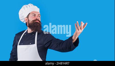 Bearded Chef maschio in uniforme, grembiule e cappello tiene un po' a portata di mano. Spazio copia per la pubblicità. Foto Stock