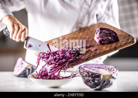 Cavolo rosso grattugiato a piccole strisce messo da un tagliere in una ciotola. Foto Stock
