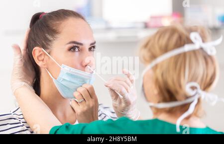 Il medico sta assumendo il test del coronavirus con un tampone su una paziente con maschera facciale. Foto Stock