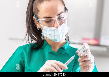 Il medico che indossa una maschera protettiva, guanti e occhiali prende una dose per la vaccinazione contro il coronavirus in un'iniezione. Foto Stock