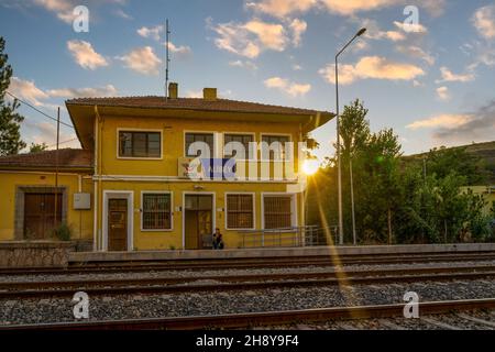 Kalecik, Ankara, Turchia - Settembre 18 2021: Vista lontana della donna passeggero in attesa al giallo edificio della stazione ferroviaria di Alibey al tramonto. Foto Stock