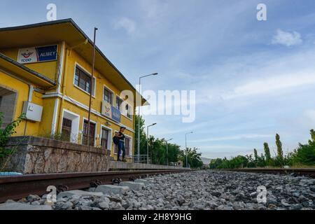 Kalecik, Ankara, Turchia - Settembre 18 2021: Vista lontana della donna passeggero in attesa al giallo edificio della stazione ferroviaria di Alibey. Foto Stock