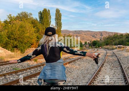 Vista posteriore della donna che allunga le braccia su binari ferroviari. Una donna in attesa di un passeggero del treno. Una donna desiderosa di una vacanza. Foto Stock