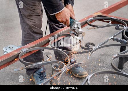 Smerigliatura in metallo con smerigliatrice angolare. Le scintille volano sui lati. Mano maschile e primo piano dello strumento Foto Stock