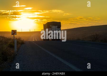 Vista posteriore del camion guida su una strada di campagna e il tramonto sullo sfondo. Foto Stock