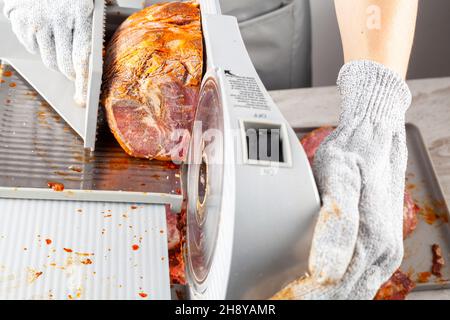 Primo piano immagine isolata che mostra un macellaio o chef affettare un grande blocco di carne surgelata. Pastirma turco, pastrama, prosciutto, manzo concetto. La persona w Foto Stock