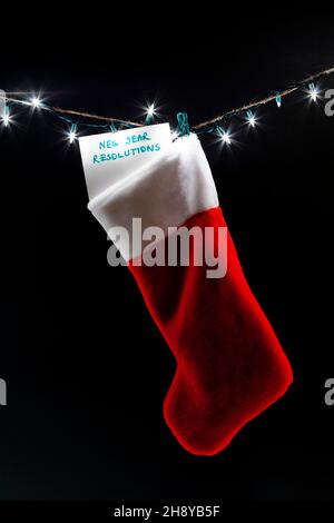 Un elenco di risoluzioni di nuovo anno è allegato ad una calza di natale appesa su una serie di luci decorative. Un'immagine di concetto di umorismo scuro per responsabile Foto Stock