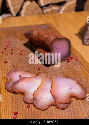 Gammon affumicato affettato su un tavolo di legno con aggiunta di erbe fresche e spezie aromatiche Foto Stock