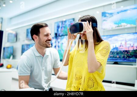 Sorridenti amici che acquistano occhiali 3d vr nel negozio di tecnologia. Vivi l'avventura del gioco virtuale. Foto Stock