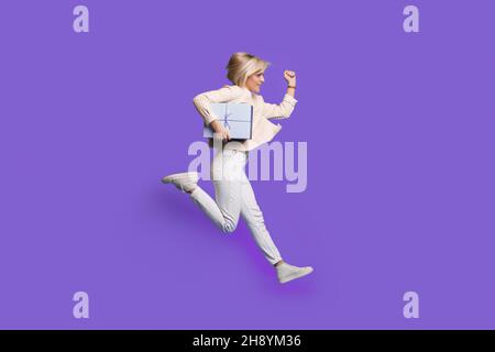 Foto del profilo completo del corpo di una donna run tenuta regalo indossare felpa e sneakers isolato su sfondo viola. Buon compleanno. Foto Stock