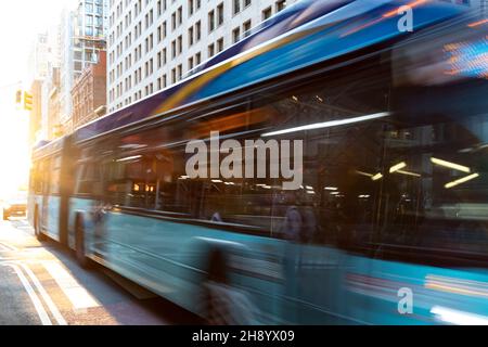 Autobus di New York City che percorrono la strada attraverso Manhattan con effetto motion blur e luce del sole che splende sullo sfondo Foto Stock