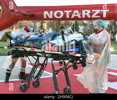 Wittenberg Lutherstadt, Germania. 2 dicembre 2021. Dall'unità di terapia intensiva Corona dell'ospedale evangelico Paul Gerhard Stift, una donna incinta che soffre di Covid 19 viene portata all'elicottero DRF dal medico di emergenza Air Rescue Alexander Kampe (r) e dal paramedico di emergenza Mario Gustke. Per ragioni mediche, la donna viene trasferita al centro prenatale dell'ospedale universitario di Halle. L'ospedale di Wittenberg ha aumentato i suoi 10 posti di terapia intensiva a 16, tutti attualmente occupati. Credit: Waltraud Grubitzsch/dpa-Zentralbild/dpa/Alamy Live News Foto Stock