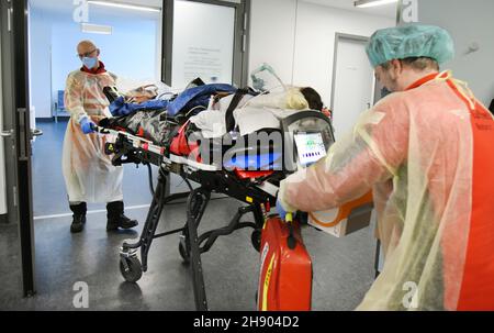 Wittenberg Lutherstadt, Germania. 2 dicembre 2021. Nell'unità di cura intensiva di Corona del Paul Gerhard Stift Evangelical Hospital, una donna incinta che soffre di covid è portata all'elicottero DRF dal medico di emergenza di salvataggio aereo Dr. Alexander Kampe (r) e dal paramedico di emergenza Mario Gustke. Per ragioni mediche, la donna viene trasferita al centro prenatale dell'ospedale universitario di Halle. L'ospedale di Wittenberg ha aumentato i suoi 10 posti di terapia intensiva a 16, tutti attualmente occupati. Credit: Waltraud Grubitzsch/dpa-Zentralbild/dpa/Alamy Live News Foto Stock