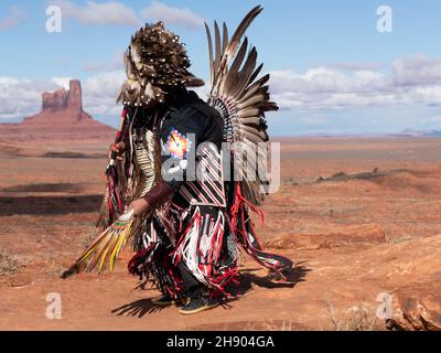 Danzatrice native americana di pow wow danzante in piena regalia con erica di piume, trambusto e giubbotto a nastro con Monument Valley sullo sfondo. Foto Stock