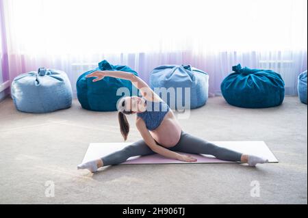 Donna europea incinta esegue esercizi con palla fitness. La madre in attesa sta facendo yoga nel 3° trimestre. Ragazza in classe in Foto Stock