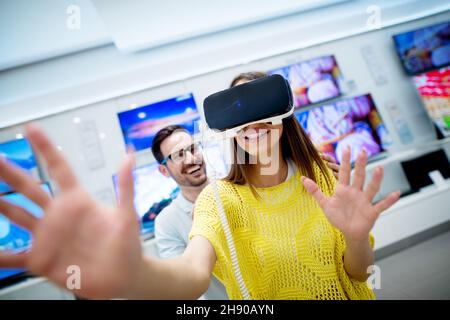 Coppia nel negozio di elettronica, esplorando gli occhiali di protezione per la realtà virtuale. Foto Stock