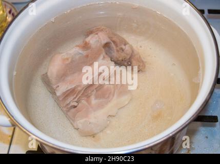 Un pezzo di carne cruda in una pentola bianca smaltata da vicino, cucinando brodo di carne fatto in casa. Foto Stock