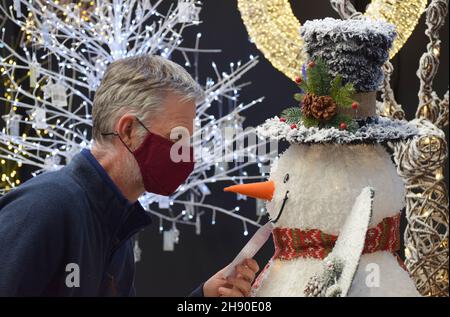 Un uomo che indossa una maschera che viene faccia a faccia con una novita' decorativo snowman come lui negozi per le decorazioni di Natale nel dicembre 2021 Foto Stock