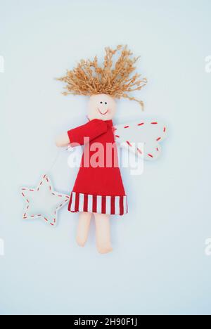 Carino Angelo di Natale fatto di tessuto isolato. Composizione di bambola sorridente con ali in abito rosso e stella su sfondo bianco. Foto Stock