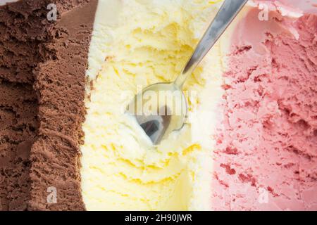 Gelato: Un cucchiaio in una grande scatola di ghiaccio con cioccolato, vaniglia e gelato alla fragola Foto Stock