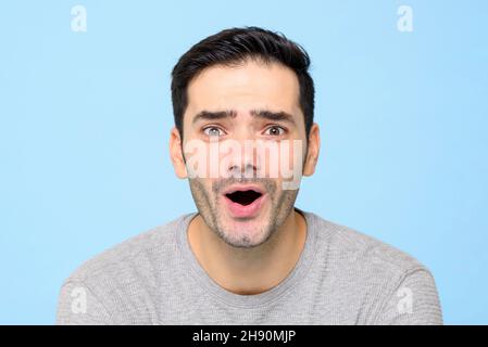 Sorprende il bell'uomo caucasico che gaspa in isolato sfondo blu chiaro studio Foto Stock