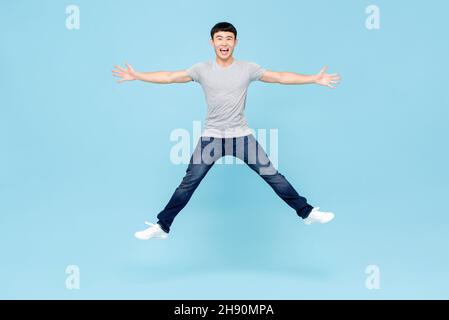 Ritratto a corpo pieno di giovane allegro e vivace uomo asiatico che salta con mani e gambe aperte in studio isolato su sfondo azzurro chiaro Foto Stock