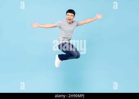 Jumping estatico giovane asiatico con le braccia che si allungano a mezz'aria isolato in blu studio sfondo Foto Stock