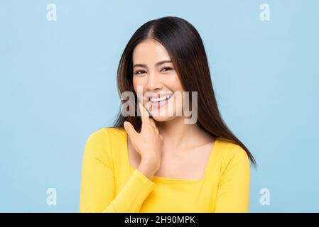 Bella sorridente giovane donna asiatica faccia in blu chiaro isolato studio sfondo Foto Stock