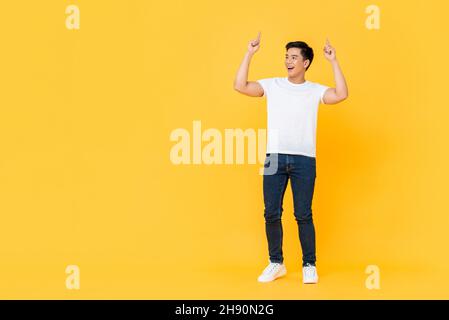 Sorridendo giovane bell'uomo asiatico guardando lo spazio vuoto e puntando due dita verso l'alto isolato su sfondo giallo studio Foto Stock
