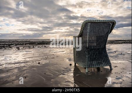 Vecchia sedia scartata e indesiderata su una spiaggia deserta nel Regno Unito. Mobili abbandonati o roba spazzatura della spiaggia che stillano una spiaggia. Foto Stock