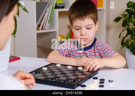 Madre e figlio giocano a dama in casa. Giochi da tavolo per bambini e bambini Foto Stock