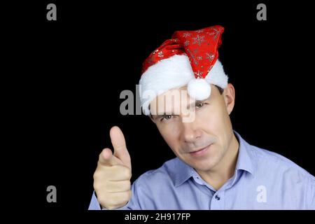 Ritratto di uomo felice in Santa Hat puntando con il dito alla fotocamera. Festa di Natale, Capodanno Foto Stock