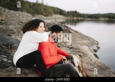 Coppia eterosessuale seduta a lakeshore durante la vacanza Foto Stock