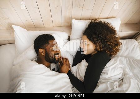 Sorridente coppia multirazziale sdraiata sul letto in cottage Foto Stock